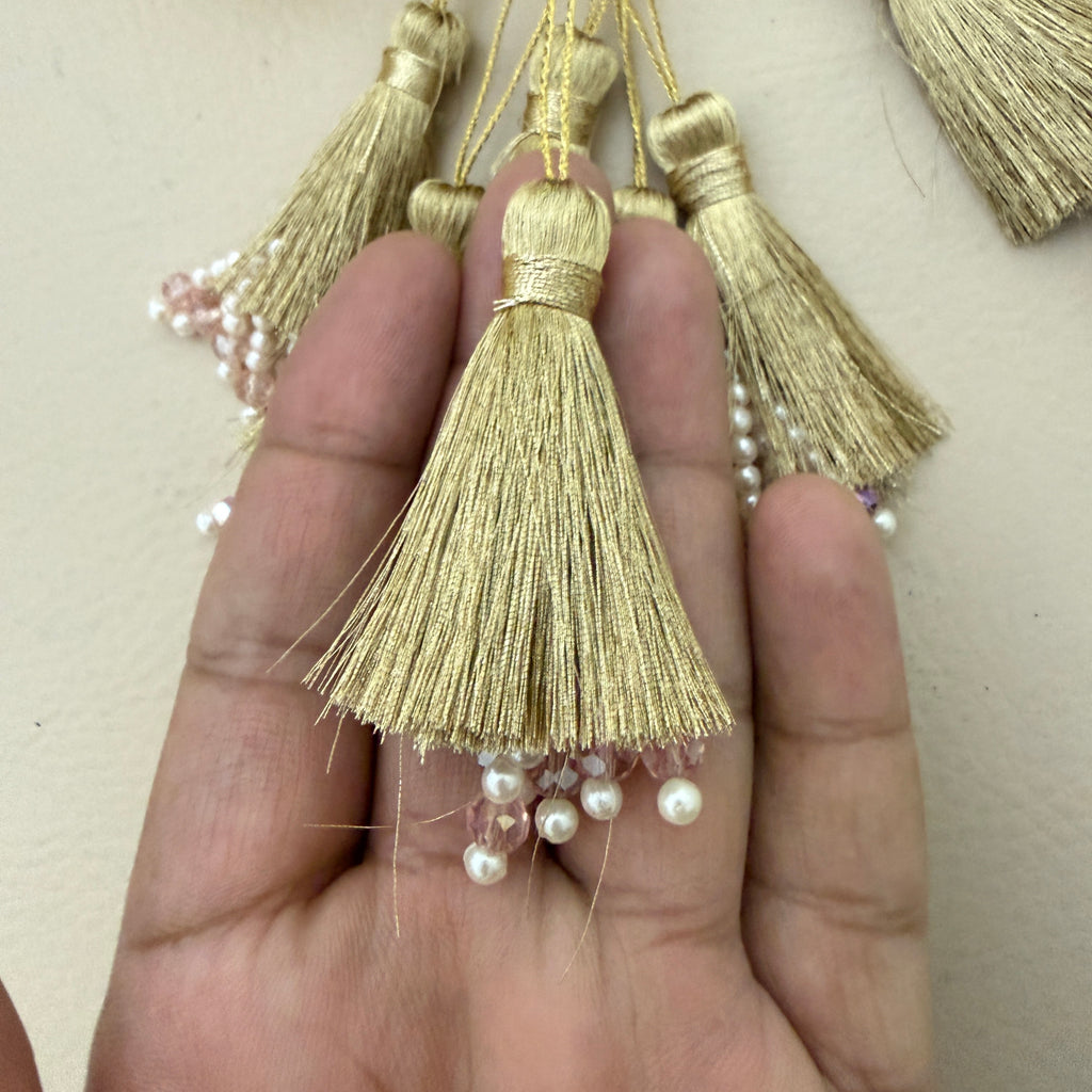 Gold tassels with pearls held between fingers against a neutral background