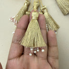 Gold tassels with pearls held between fingers against a neutral background