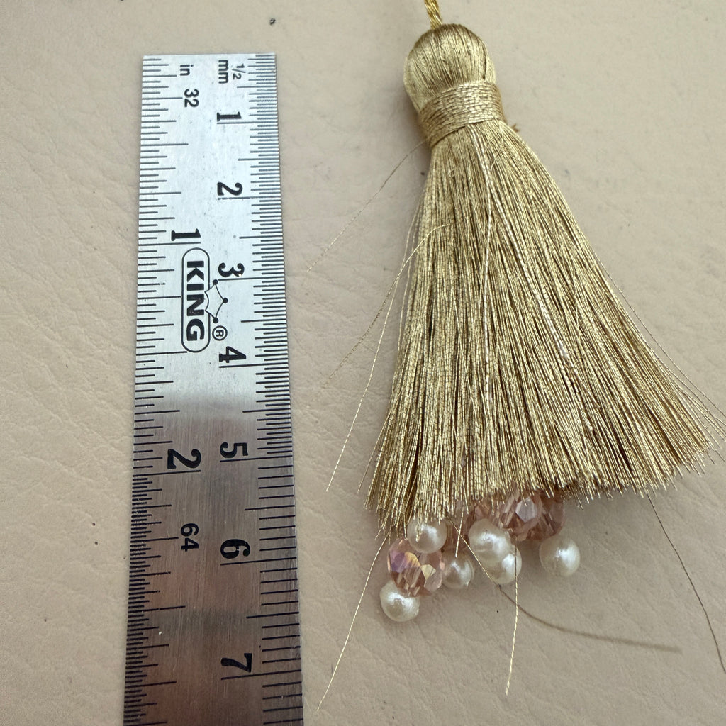 Gold tassel with beads next to a ruler on a beige background