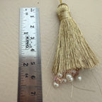 Gold tassel with beads next to a ruler on a beige background