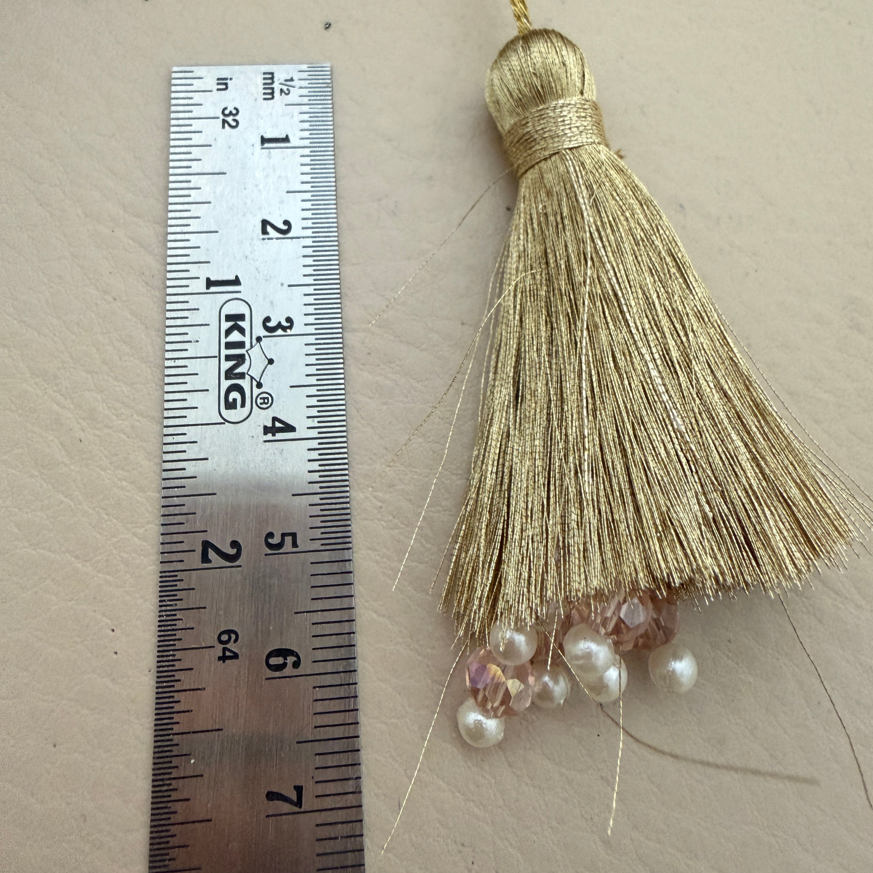 Gold tassel with beads next to a ruler on a beige background