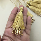 Gold tassel with beads held in a hand against a neutral background