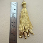 Gold tassel with beads next to a ruler on a light gray background