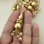 Gold beaded earring held between fingers against a neutral background