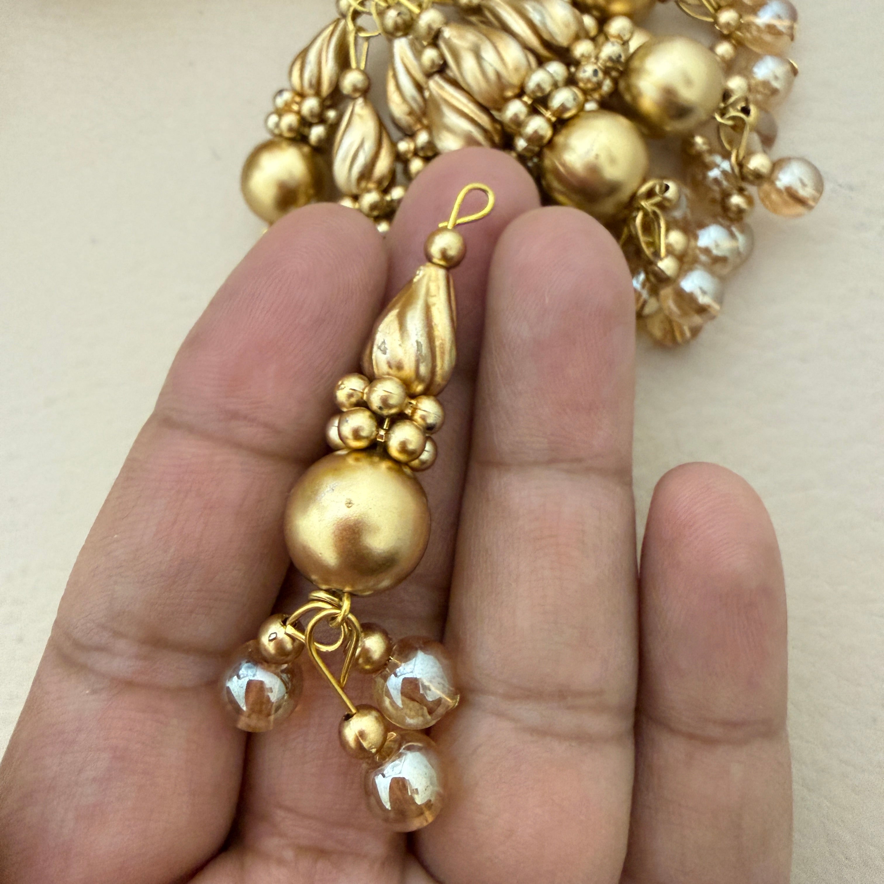 Gold beaded earring held between fingers against a neutral background