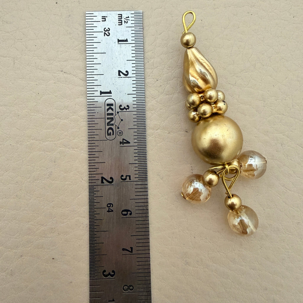 Gold decorative pendant next to a ruler on a beige background