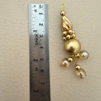 Gold decorative pendant next to a ruler on a beige background