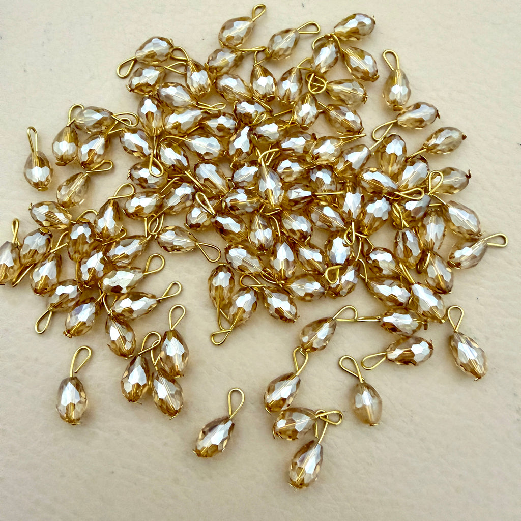 Gold and silver teardrop-shaped jewelry components on a beige background