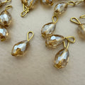 Gold and clear teardrop-shaped jewelry components on a beige surface