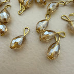 Gold and clear teardrop-shaped jewelry components on a beige surface