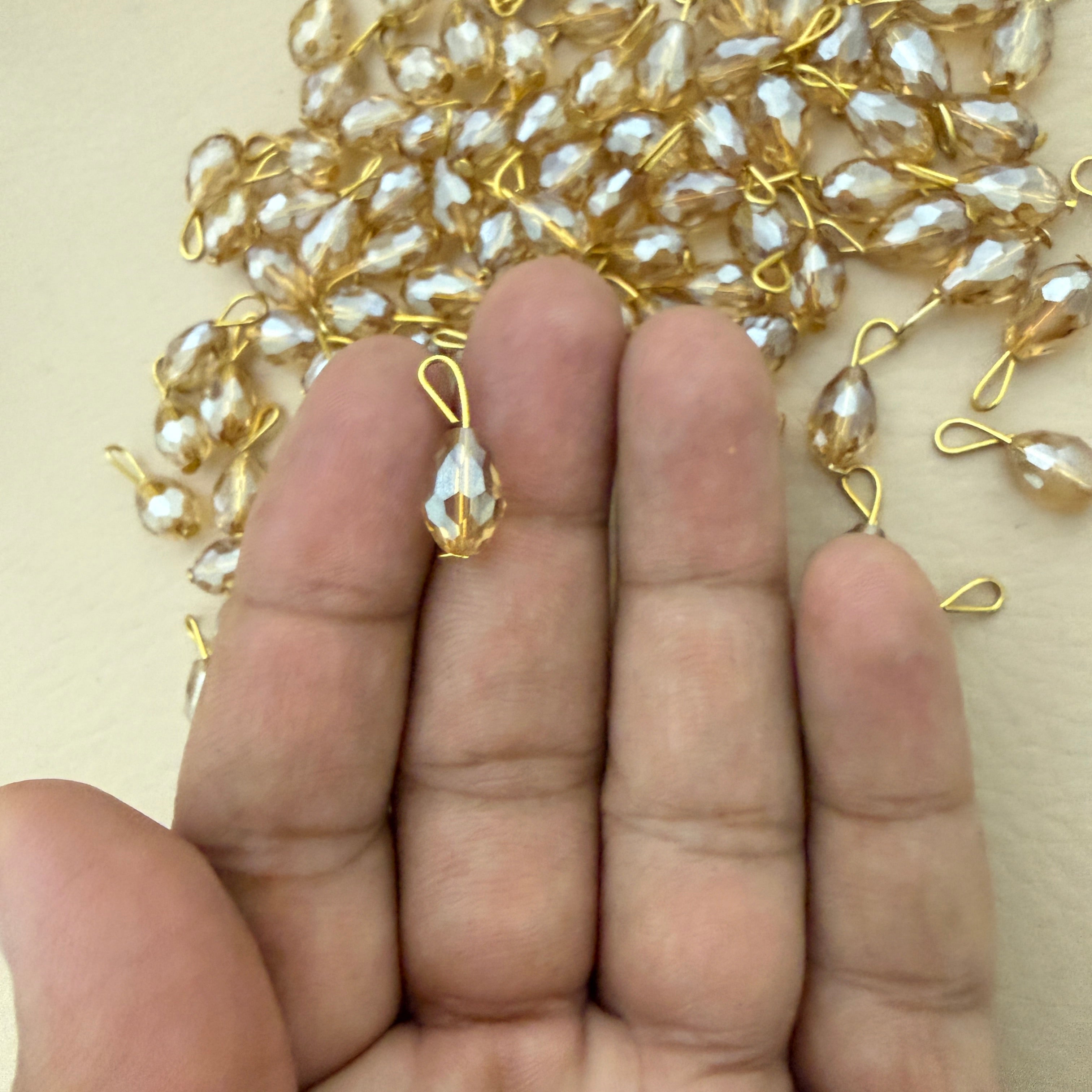Gold and pearl jewelry components on a hand with a beige background