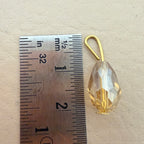 Gold teardrop-shaped pendant next to a ruler on a beige background