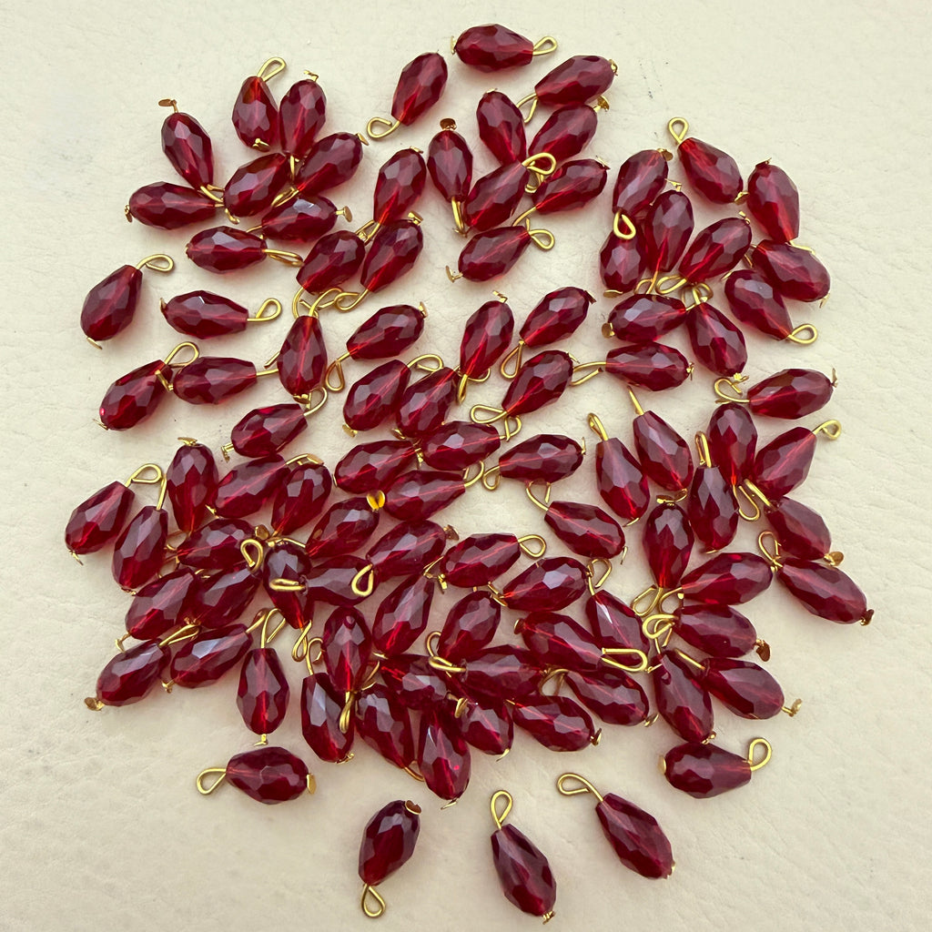 Red teardrop-shaped beads with gold loops on a beige background