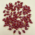 Red teardrop-shaped beads with gold loops on a beige background