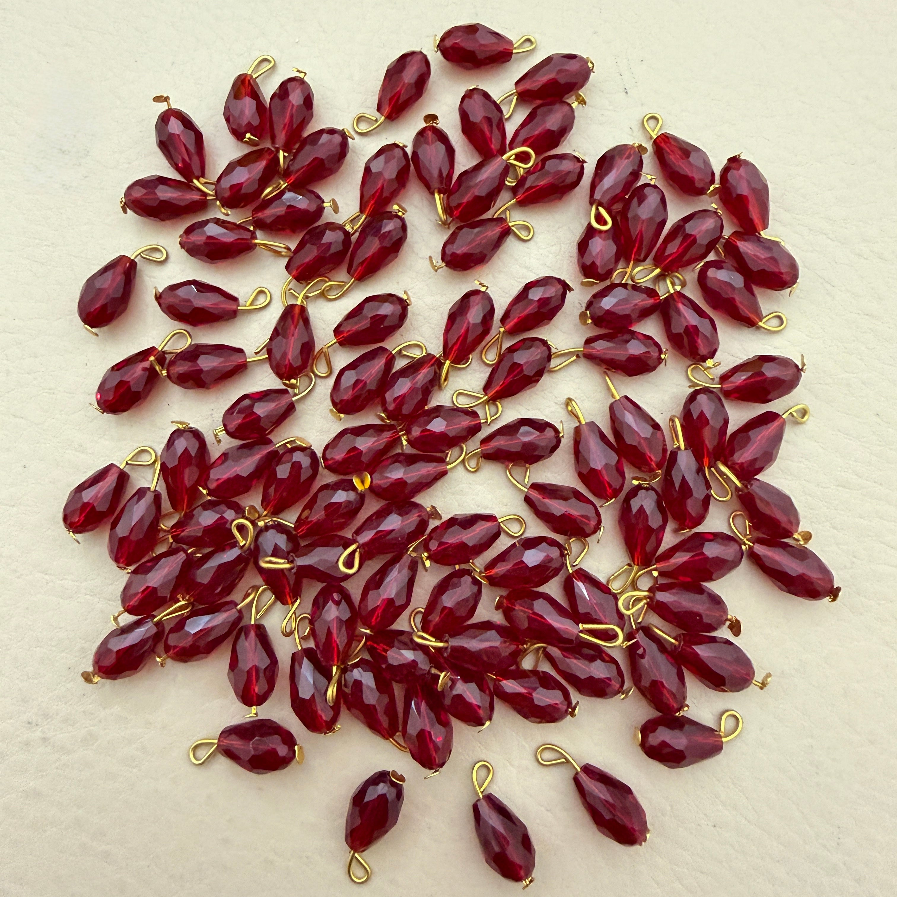 Red teardrop-shaped beads with gold loops on a beige background