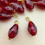 Red teardrop-shaped beads with gold loops on a light beige surface