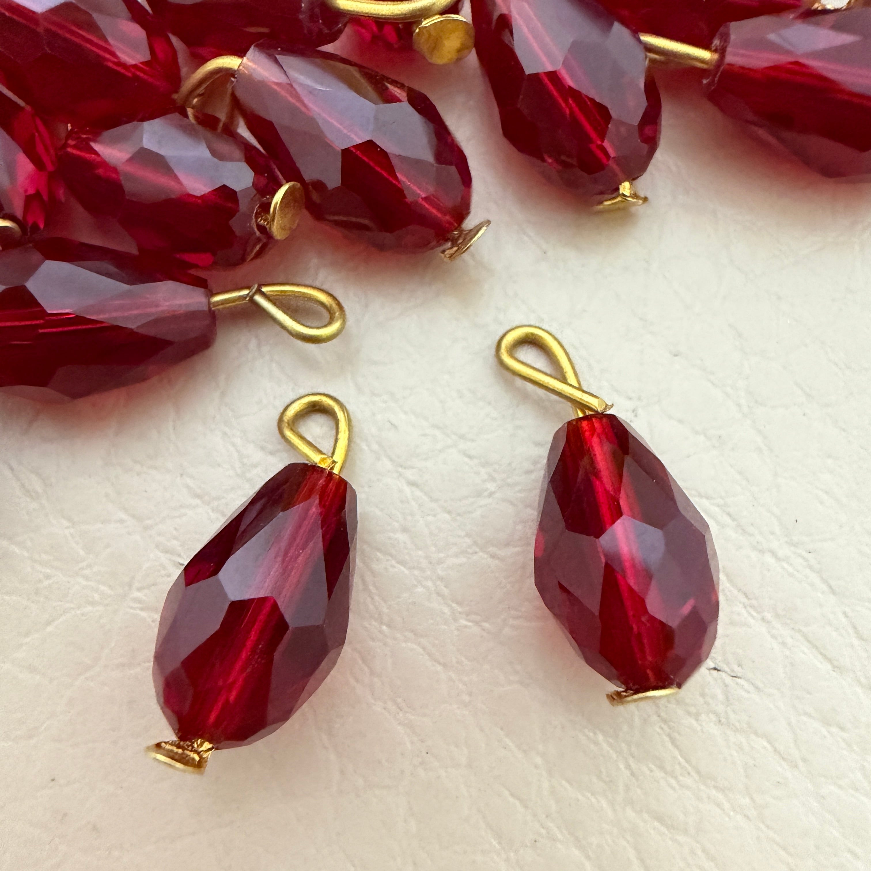 Red teardrop-shaped beads with gold loops on a light beige surface