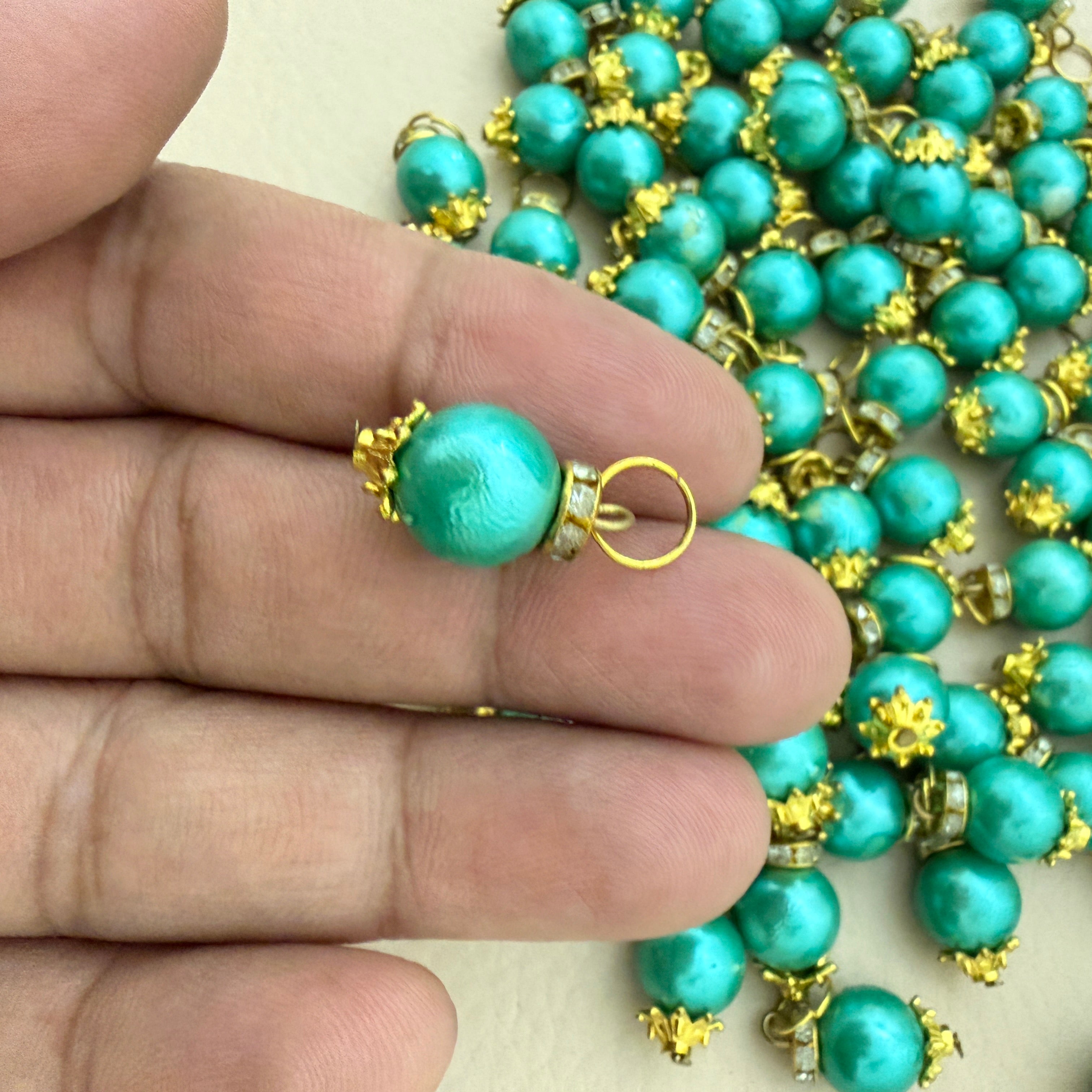 Turquoise pearl necklace with gold accents held by a hand