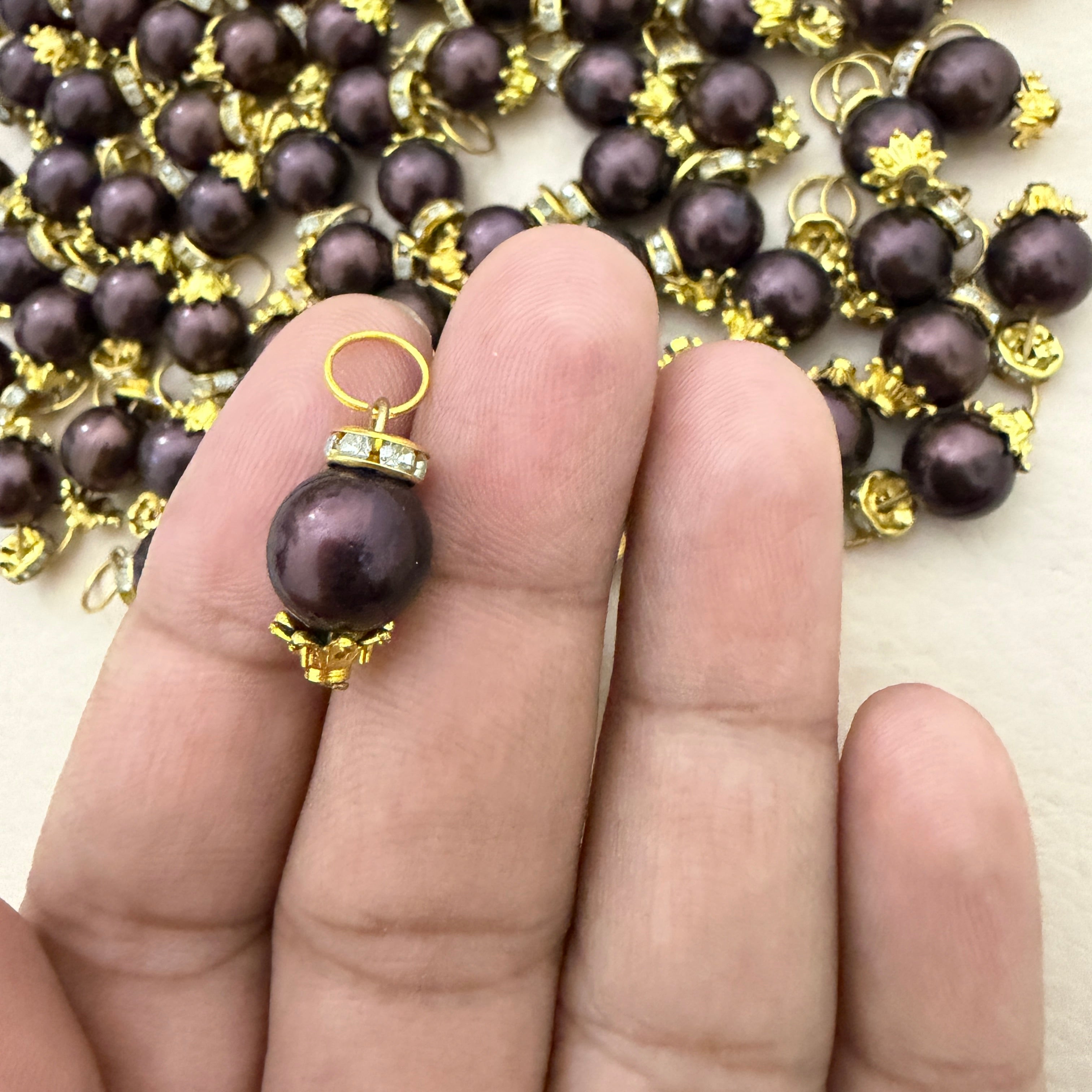 Pearl earring with gold setting held between fingers, pearl necklace in the background