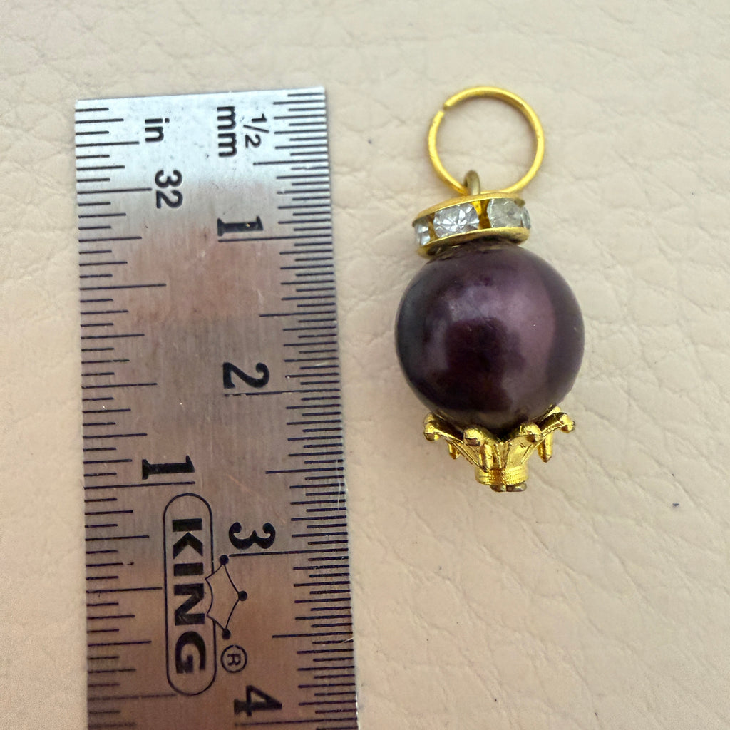 Pearl pendant with gold setting next to a ruler for scale on a beige background