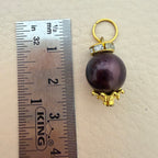 Pearl pendant with gold setting next to a ruler for scale on a beige background