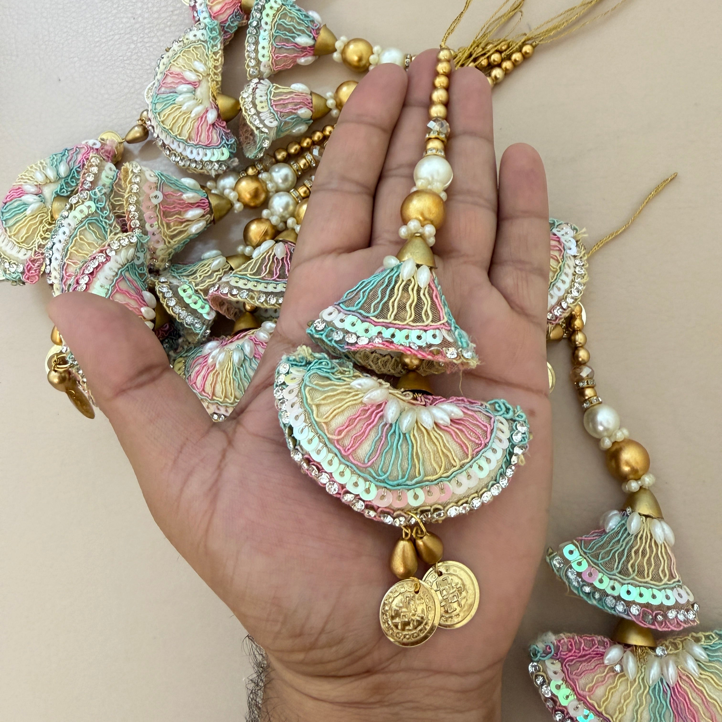 Decorative jewelry with tassels and beads held in a hand against a neutral background
