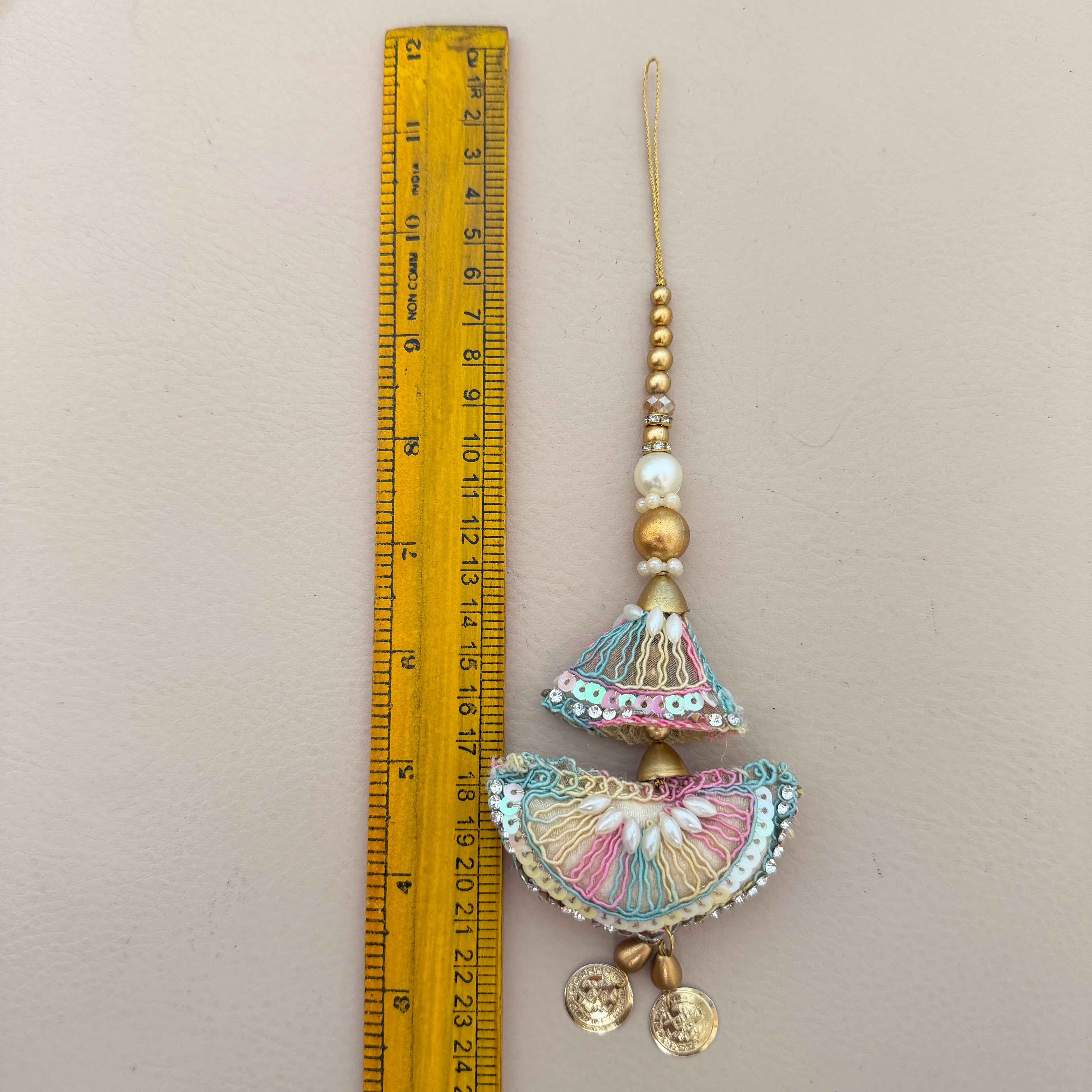Decorative hanging ornament next to a ruler on a beige background