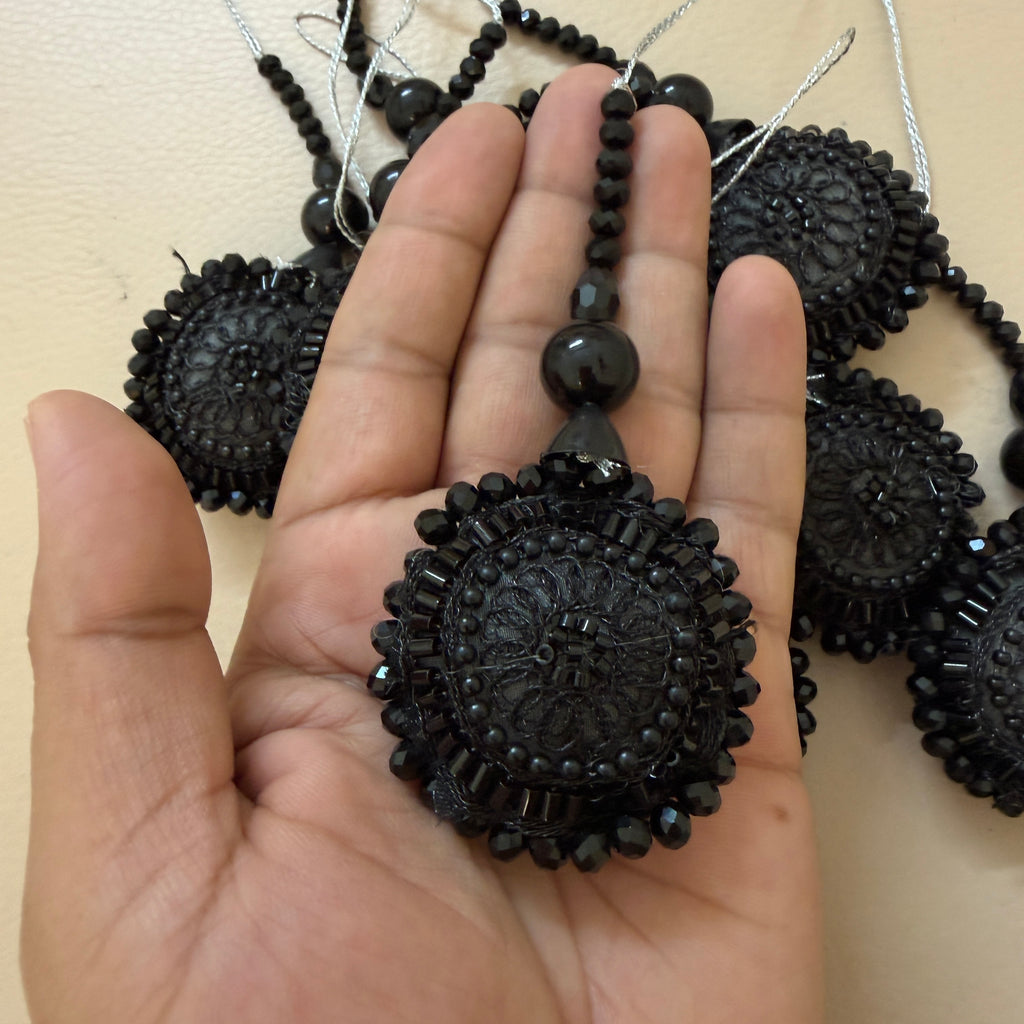 Black beaded pendant held in a hand with more pendants in the background