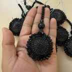 Black beaded pendant held in a hand with more pendants in the background