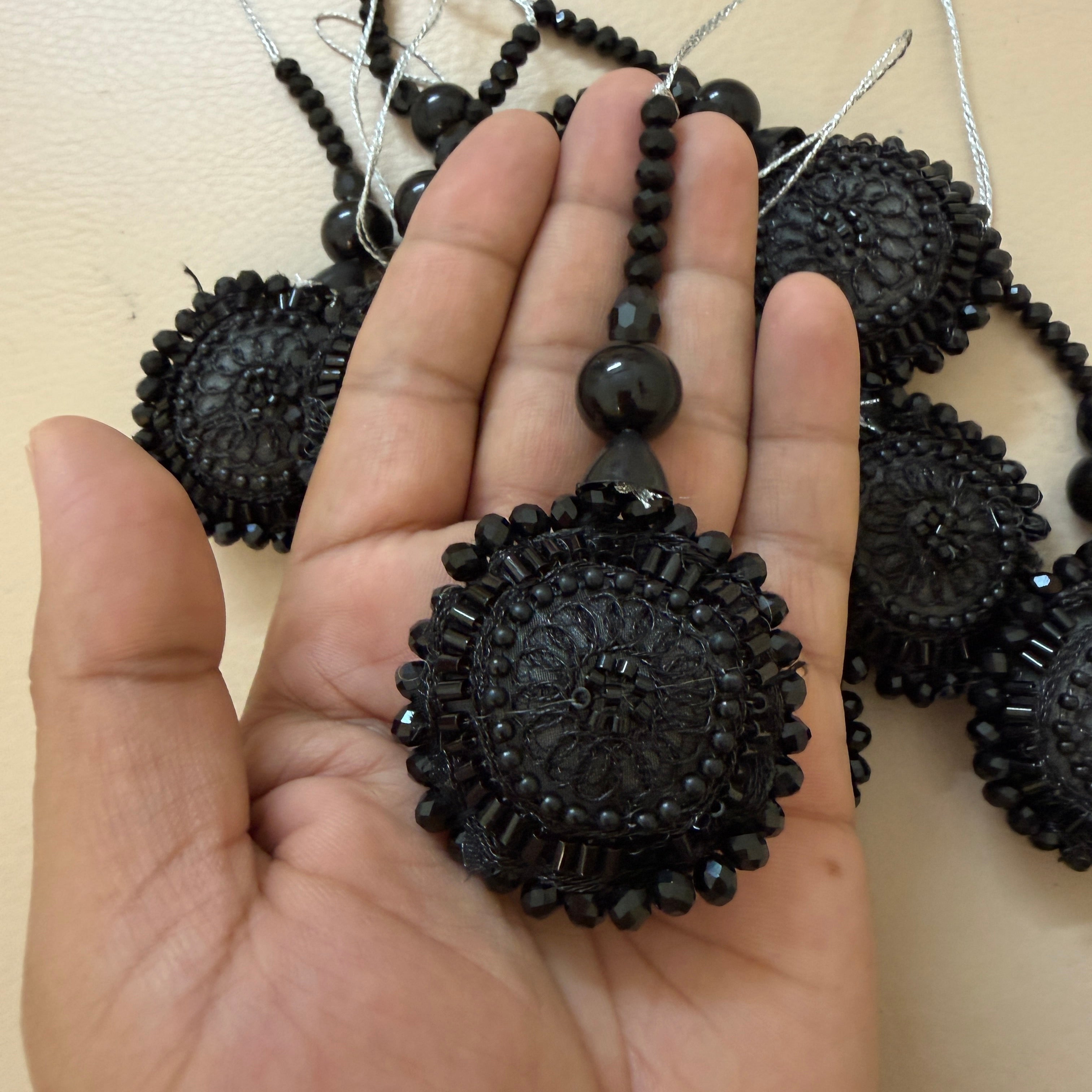 Black beaded pendant held in a hand with more pendants in the background