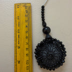 Black beaded decorative item next to a ruler on a beige background