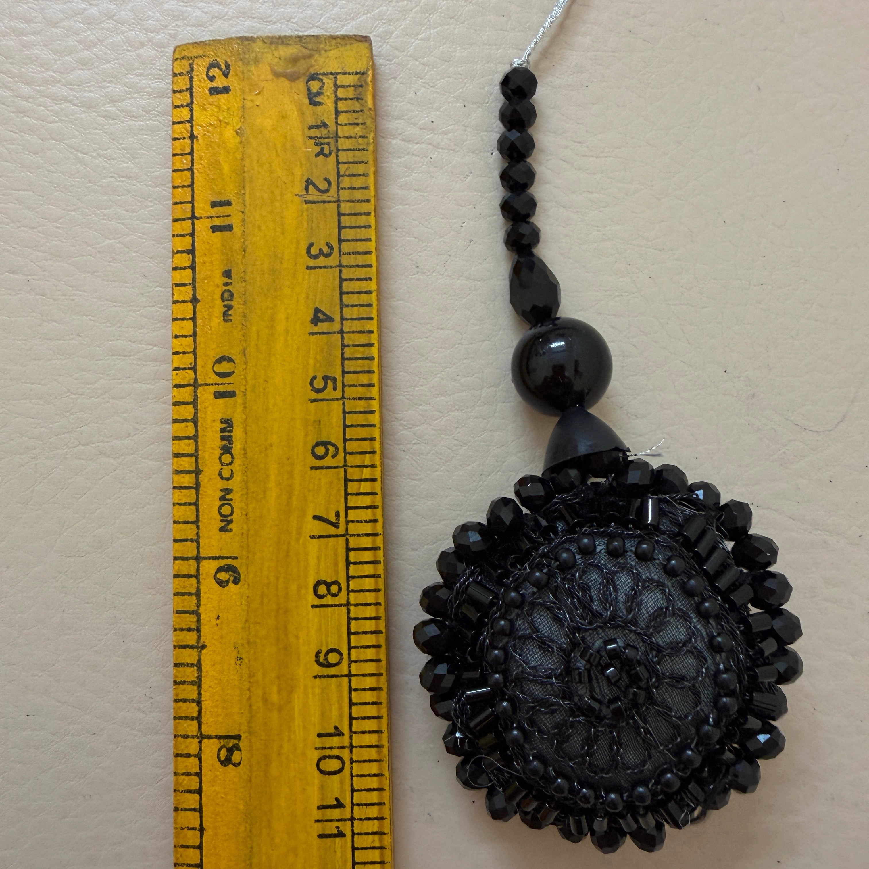 Black beaded decorative item next to a ruler on a beige background
