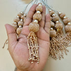 Gold beaded tassels held in a hand with additional tassels on a light background