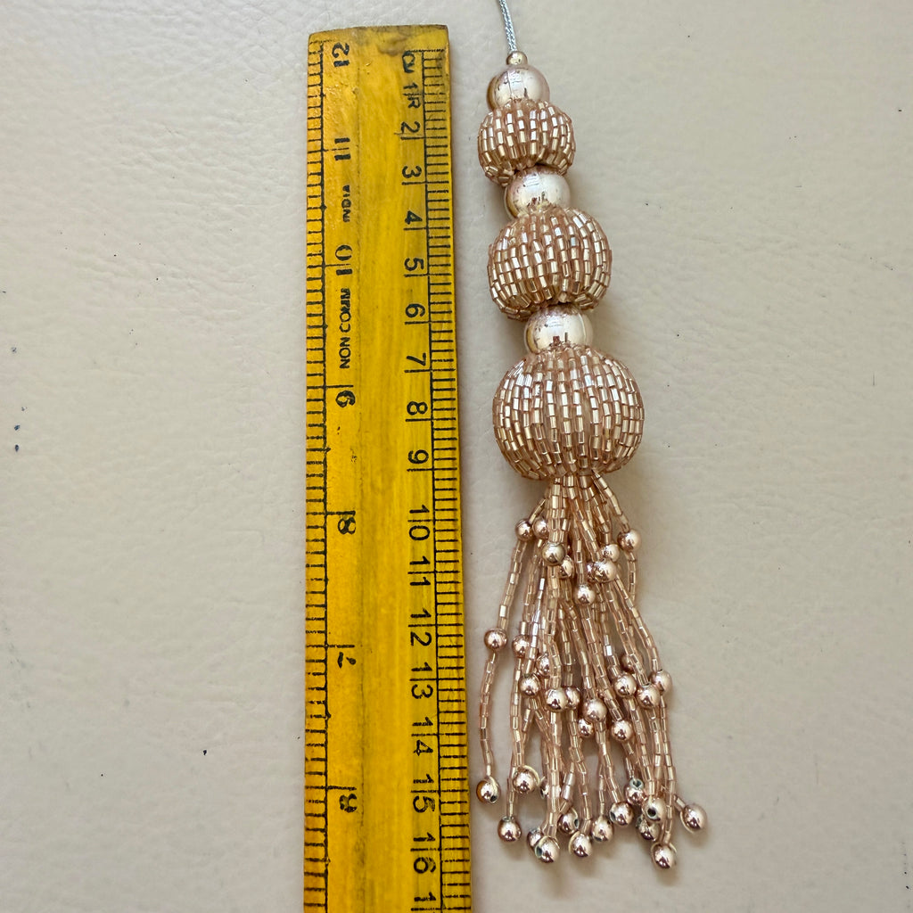 Decorative tassel with beads next to a ruler on a light gray background