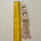 Decorative tassel with beads next to a ruler on a light gray background