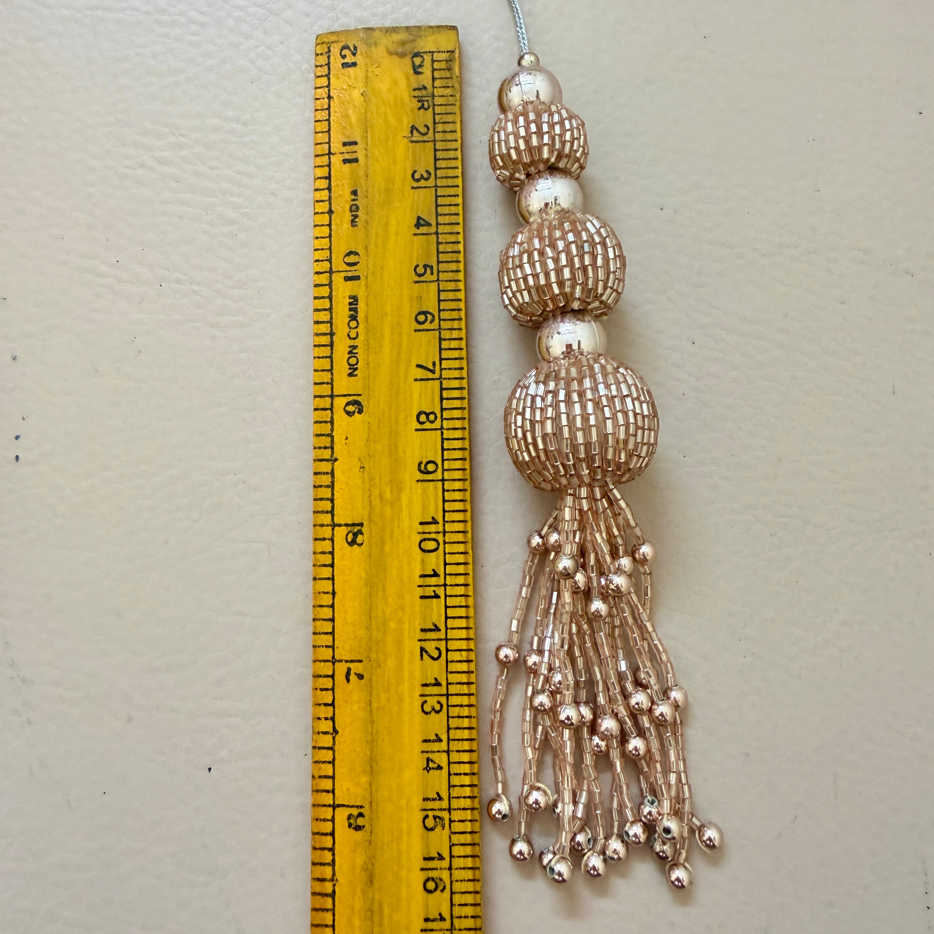 Decorative tassel with beads next to a ruler on a light gray background