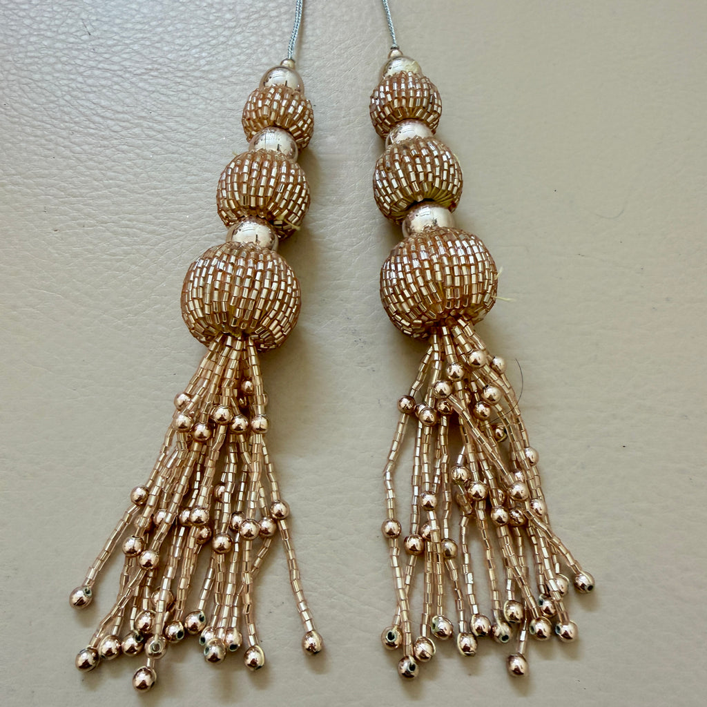 Pair of gold beaded tassel earrings on a light gray background