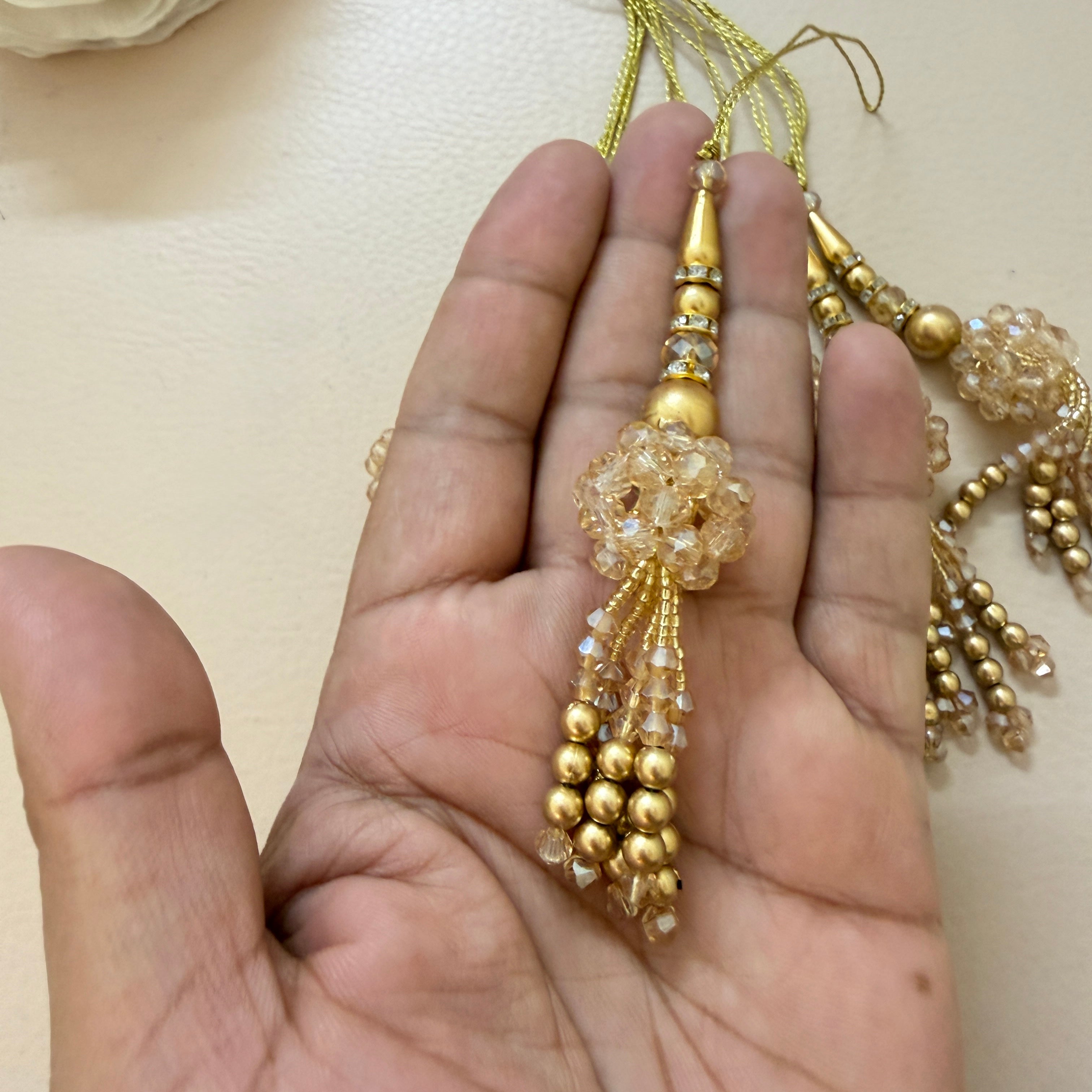 Gold necklace with tassels held in a hand against a beige background