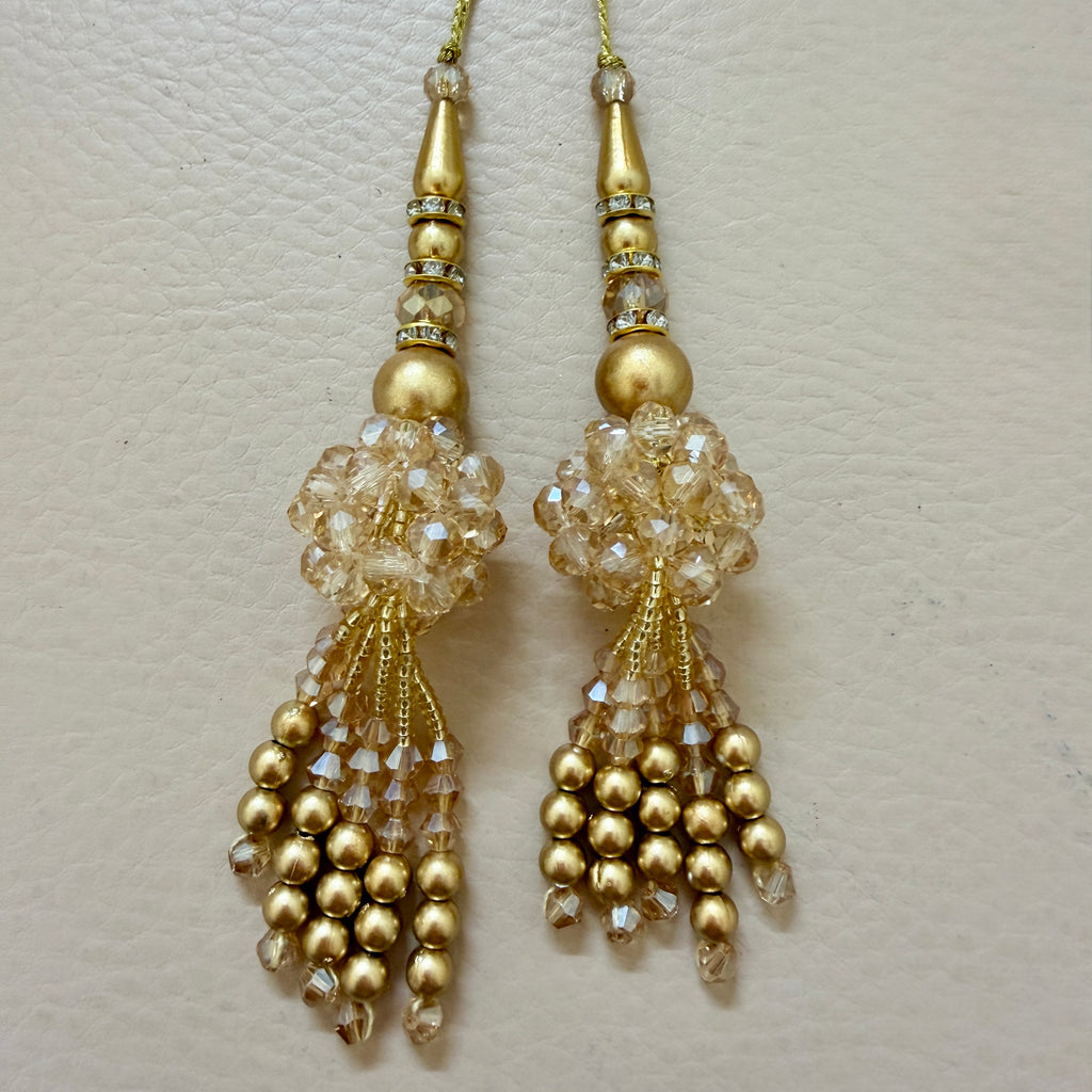Decorative gold pendant with beads and crystals next to a ruler on a light gray background