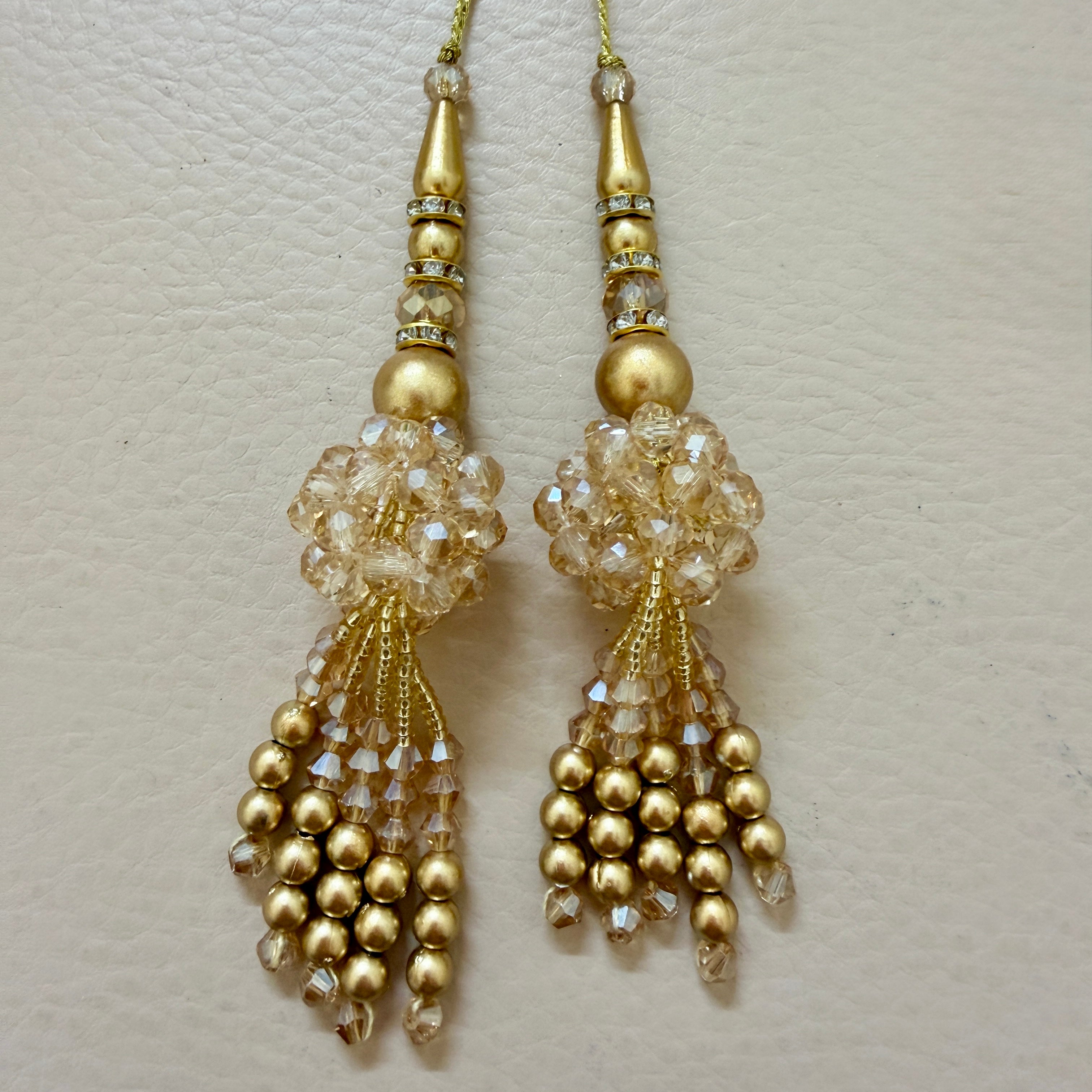 Decorative gold pendant with beads and crystals next to a ruler on a light gray background