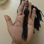 Black beaded hair tie held in a hand against a beige background