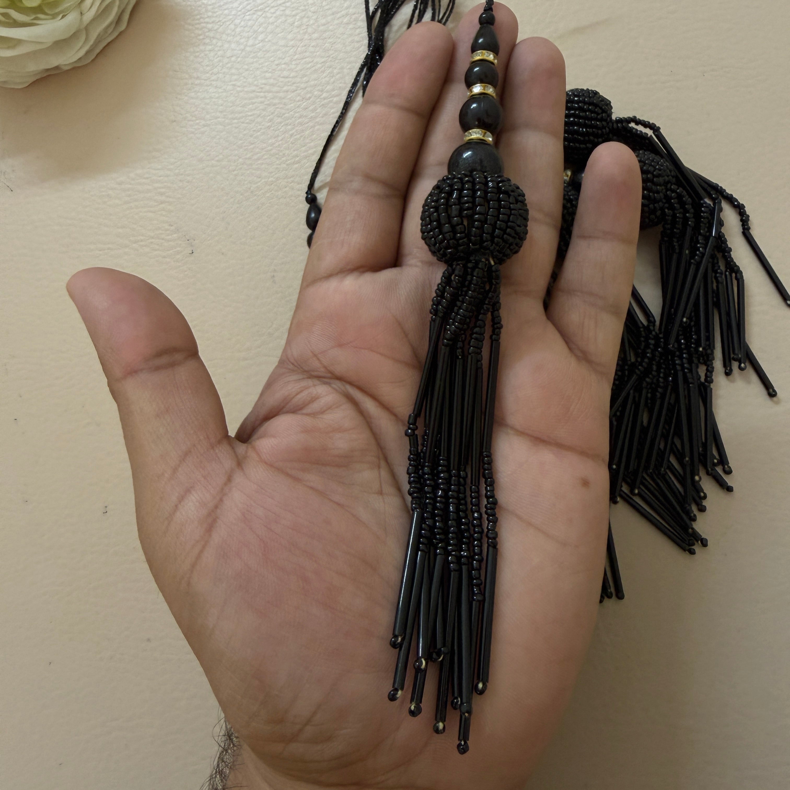 Black beaded hair tie held in a hand against a beige background
