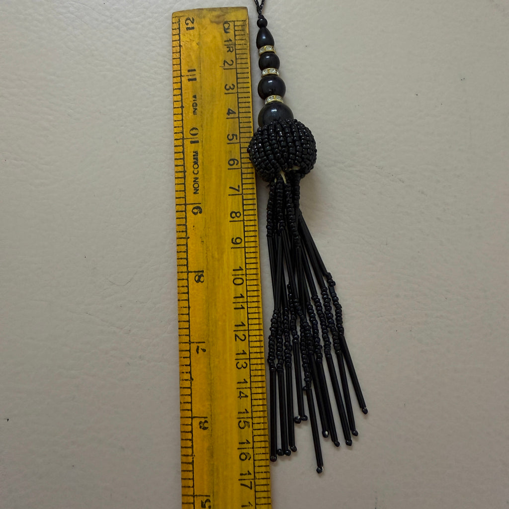 Black beaded tassel with a ruler for scale on a white background