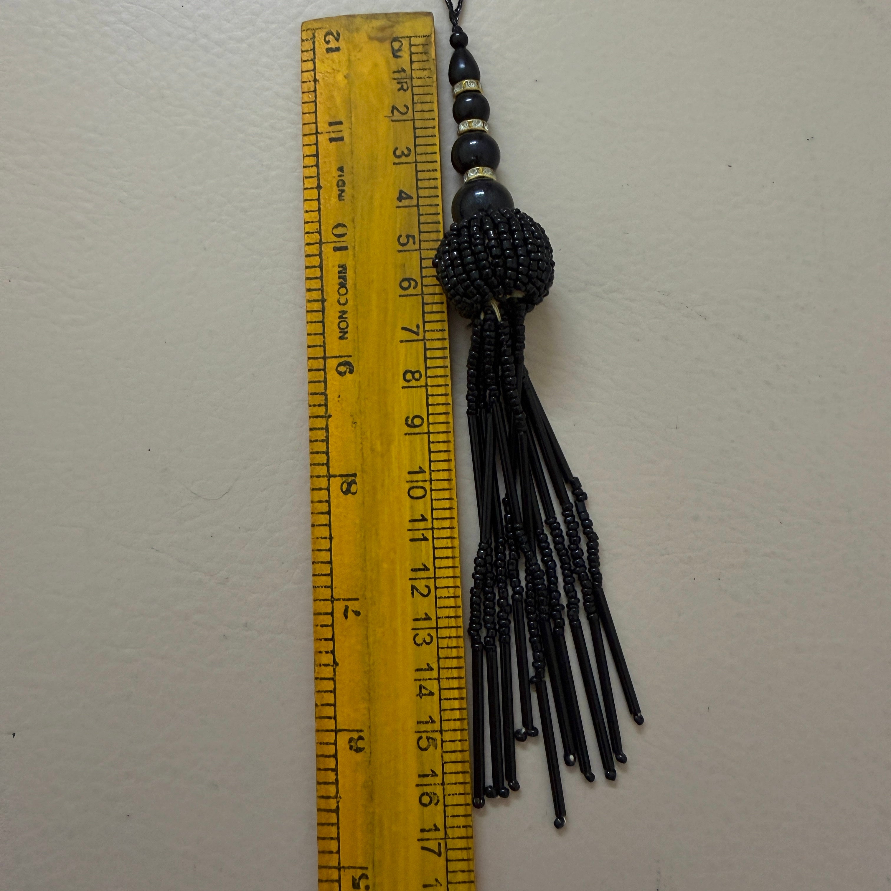 Black beaded tassel with a ruler for scale on a white background