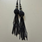 Black beaded tassel necklace on a light gray background