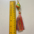 Colorful tassel with decorative ball next to a ruler on a light gray background