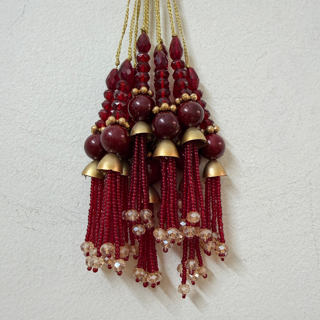 Decorative hanging with red beads and gold accents on a light gray background