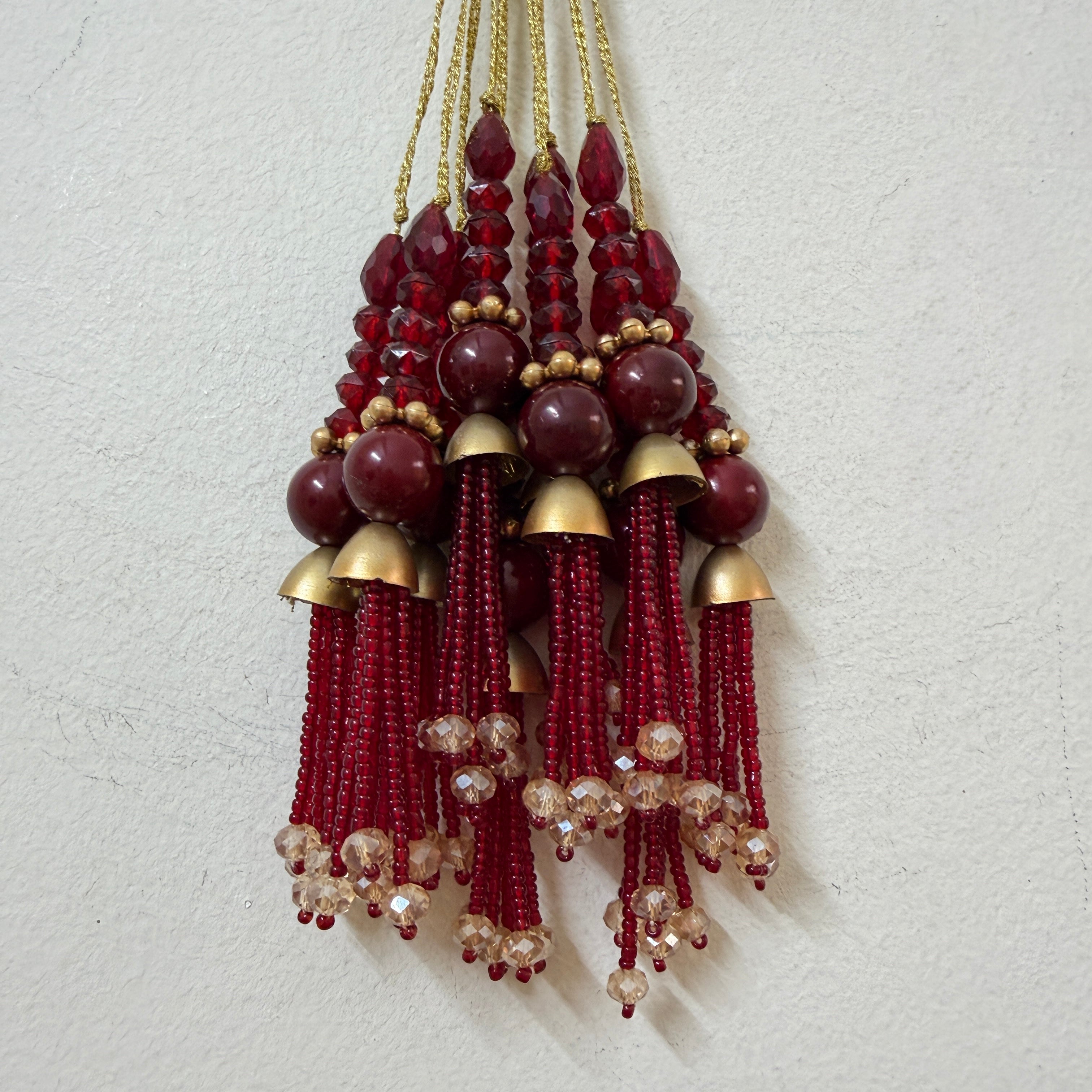 Decorative hanging with red beads and gold accents on a light gray background