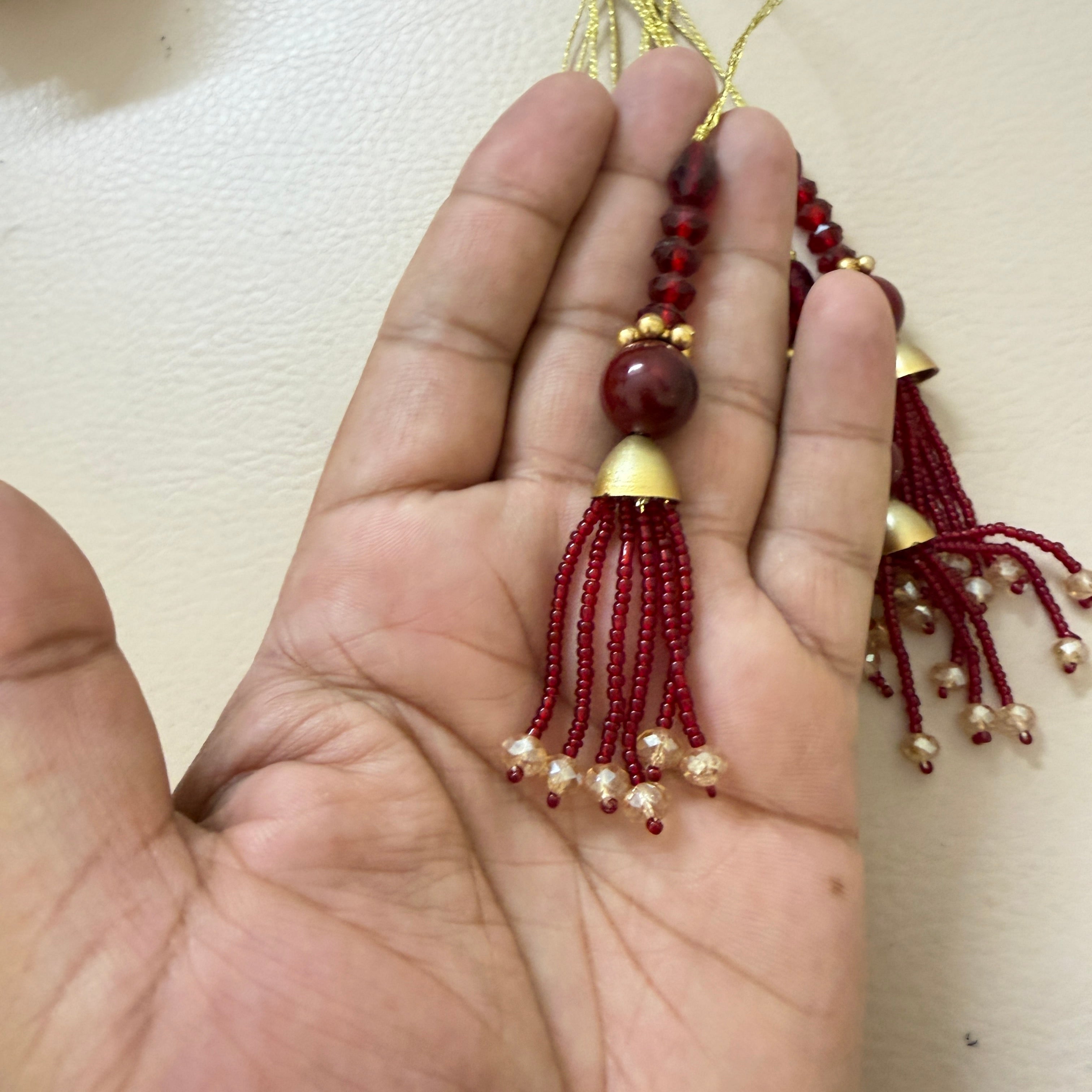 Hand holding a red beaded tassel with gold accents against a beige background