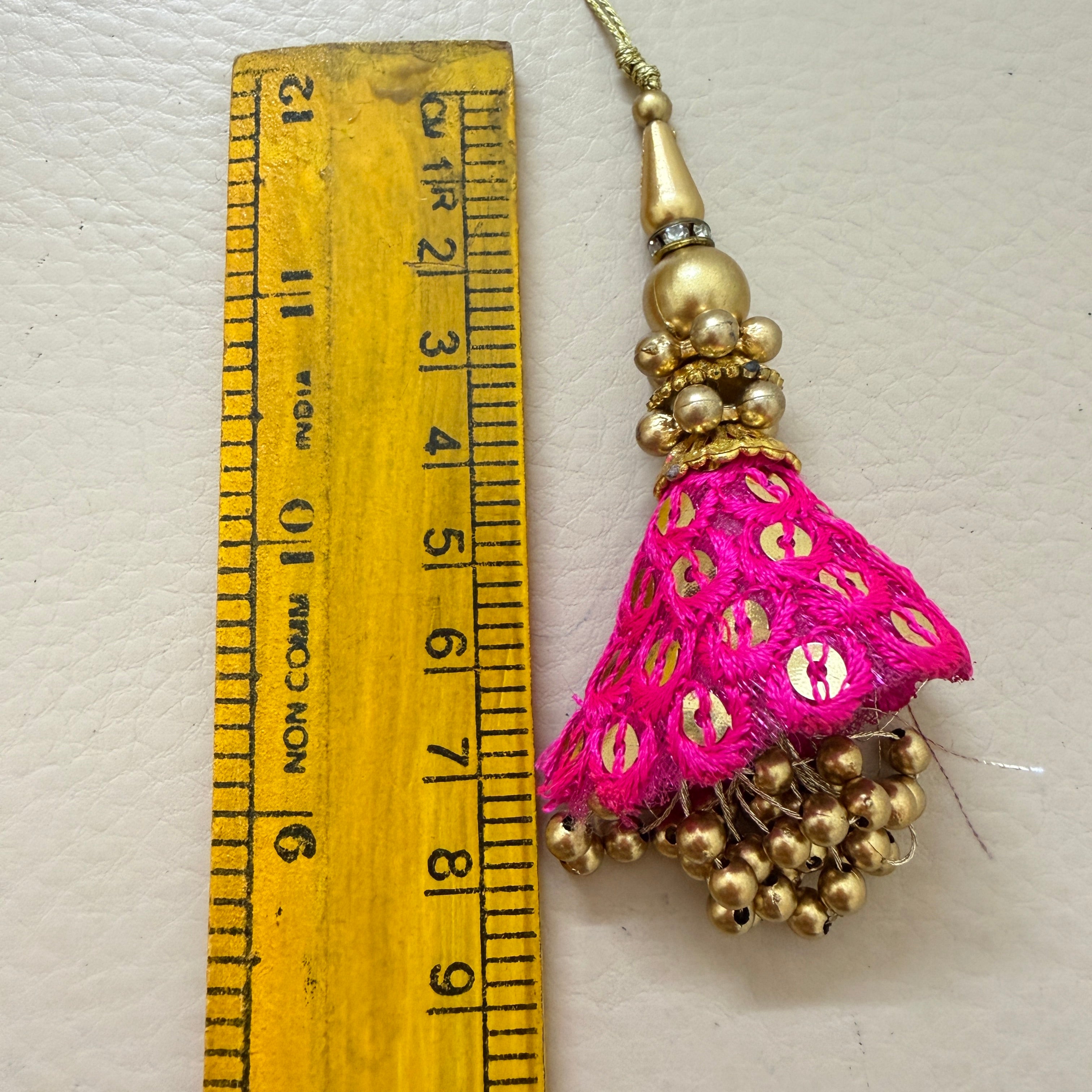 Pink tassel with gold beads next to a ruler on a light background
